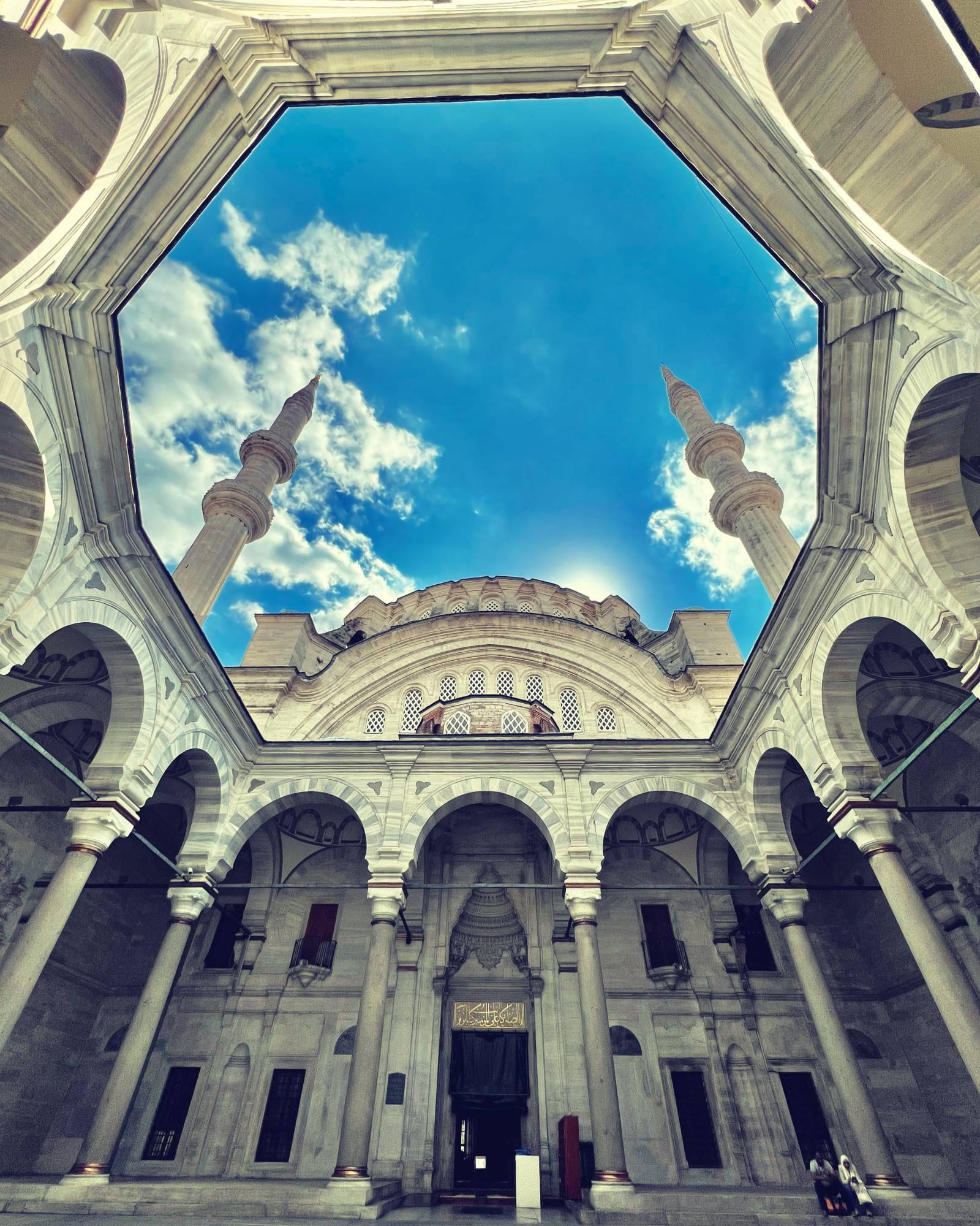 Visitors walking peacefully through a sunlit mosque courtyard in Istanbul, framed by arches and domes